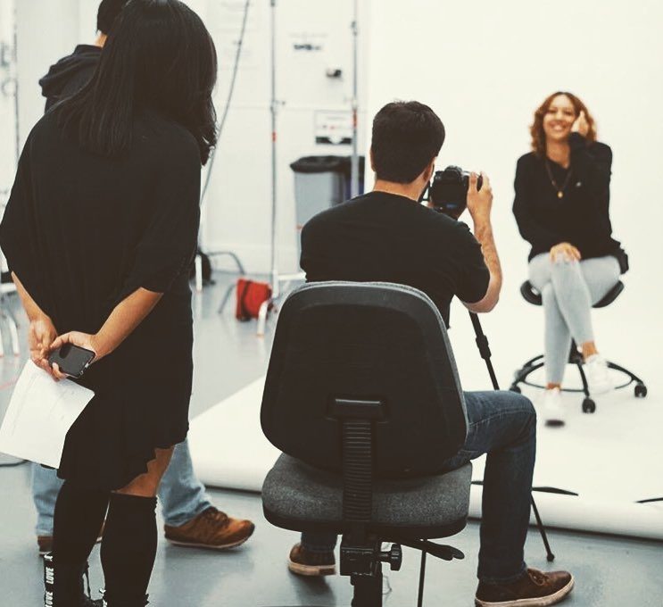 A photographer shooting a seated subject on a studio cyclorama while two crew members watch.