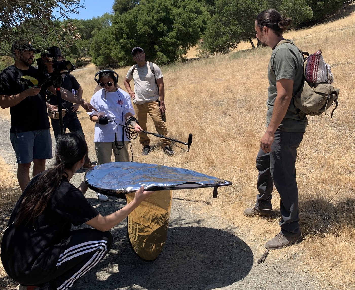 A production team shooting outdoors on a hillside with a boom mic and reflector.